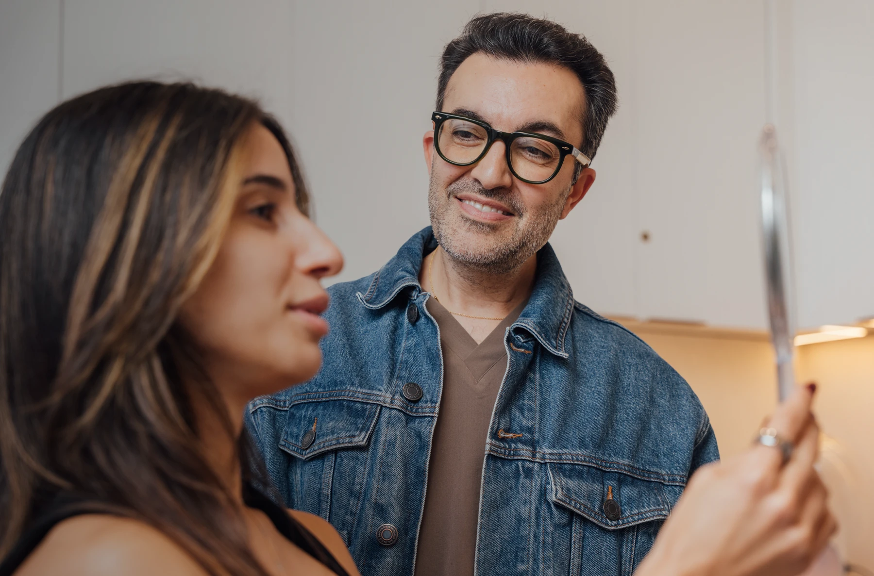 Dr. Moradzadeh, wearing a jean jacket, shown examining a patient. The patient has brown hair and is holding a mirror in front of her. - Doctor meet in Santa Barbara, CA
