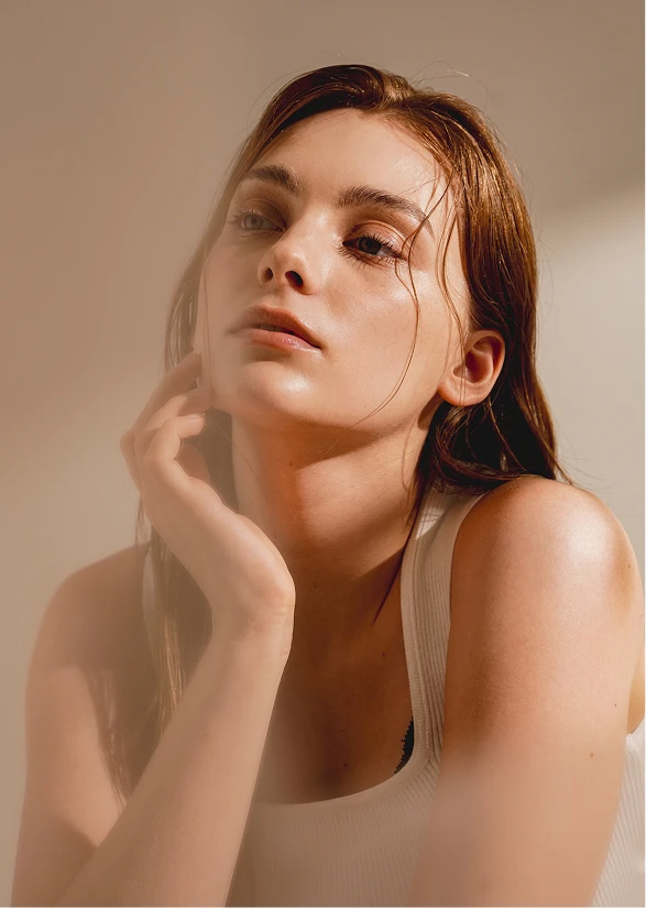 A women with red hair leans forward and looks to the left of the image. She is wearing a white tank top and her hand rests on her jaw. - Septoplasty in Santa Barbara, CA