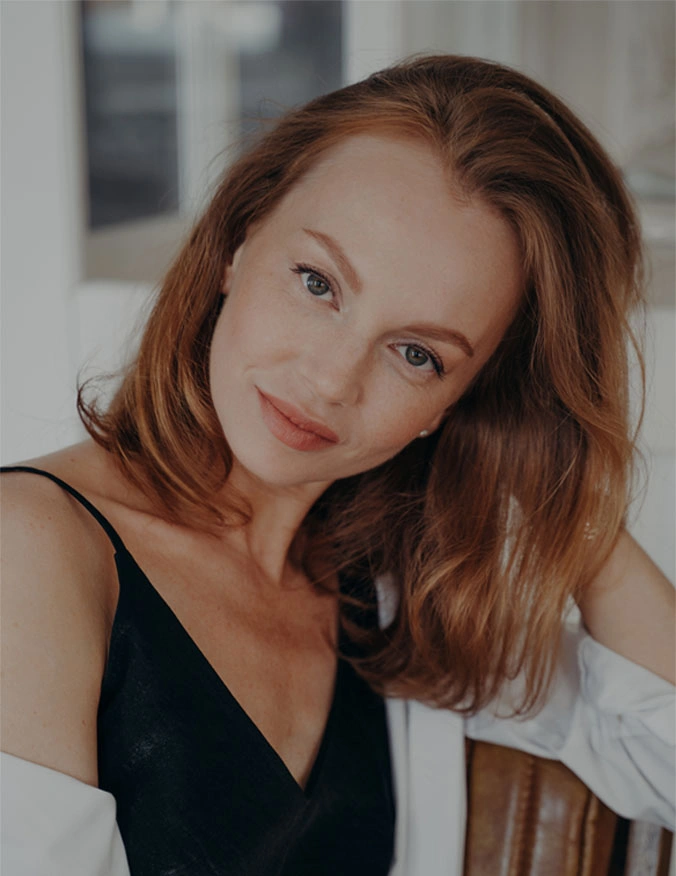 A close up of a women with red hair and light eyes. She has a slight smile on her face and wears a black tank top with a white button up shirt over. - Balloon Sinuplasty in Santa Barbara, CA