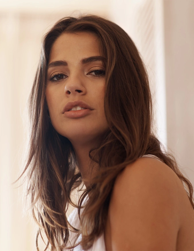 A close up of a girl looking into camera. She has mid length brown hair and brown eyes. Her mouth is slightly open and she wears a white sleeveless blouse. C02 Laser Resurfacing in Santa Barbara, CA