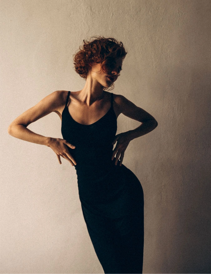 A women posed in the center of the photo wearing a black strap dress. She has a short brown curly bob and is against a concrete background. - Coolsculpting in Santa Barbara, CA