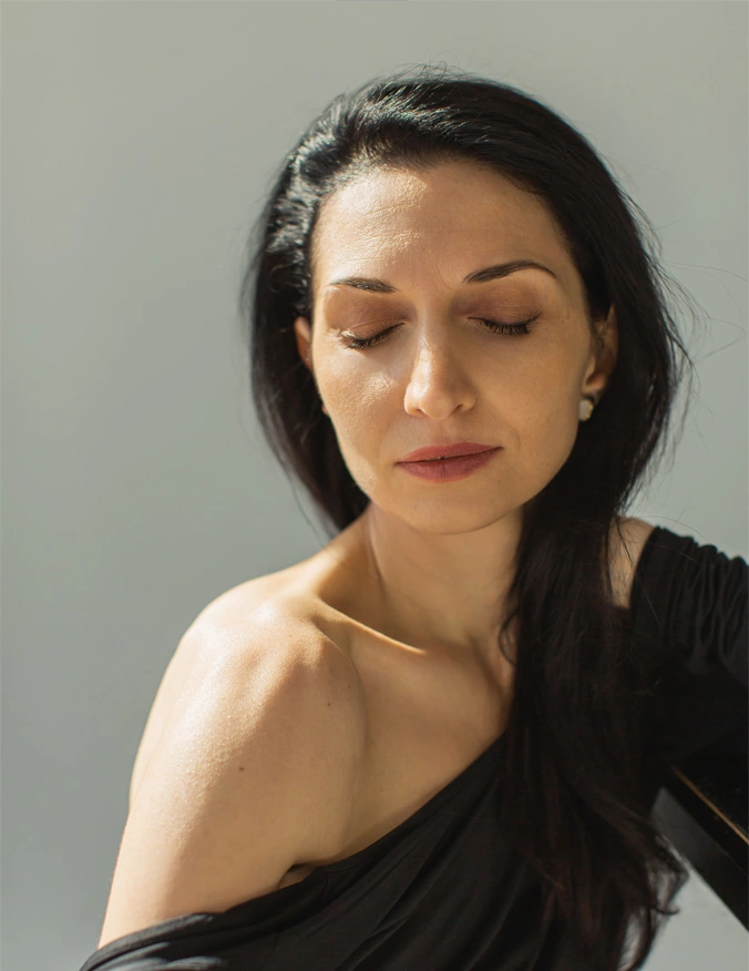 A women wearing a black off the shoulder top. She has her eyes closed and is facing towards the camera. She has black hair that is pulled behind her ears. - PRP and Exosomes for Hair Growth in Santa Barbara, CA