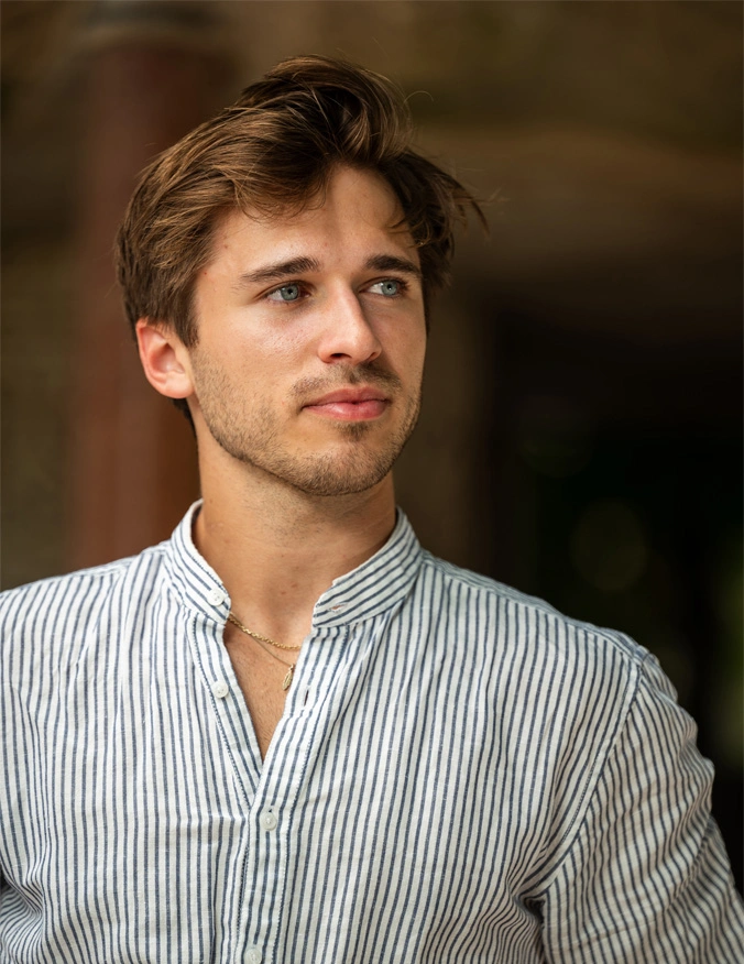 A man looks to the right of the image and is wearing a vertical striped button up shirt. He has short brown flowy hair and light green eyes. He also has stubble and a slight smirk. - Vivear Treatment in Santa Barbara, CA