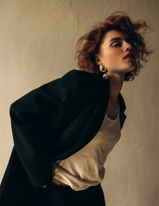 A women hunches over to the right of the image. She has short red curly hair and is wearing large hanging earrings. She has on a black blazer and a white tank top. - Biostimulators in Santa Barbara, CA