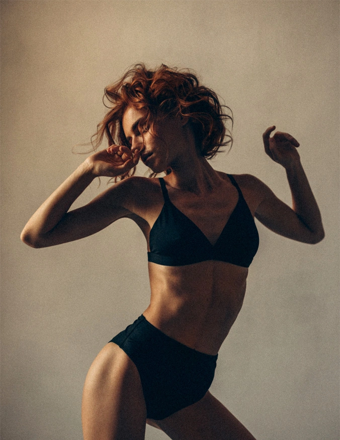 A women poses in black bra and underwear. She has short red curly hair and has her eyes closed. Her head is turned to the left side of the image. - Cellulite Treatment in Santa Barbara, CA