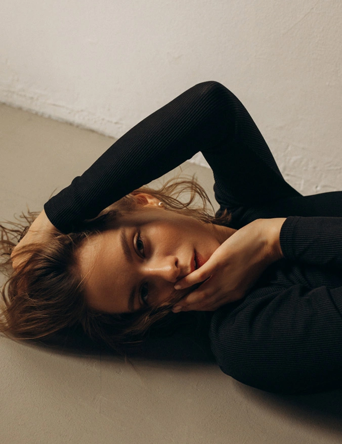 A image of a women laying on her back wearing a long black sleeve shirt. Her eyes are open as on hand holds her cheek and the other goes back behind her head and into her hair. - Diamond Glow in Santa Barbara, CA