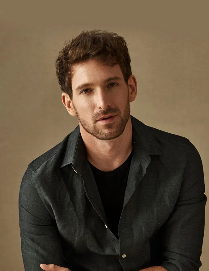 A man located in the center of the photo wearing a black shirt with a black button up long sleeve shirt. The man is looking directly at the camera and has brown short hair with a thin beard and mustache. - Earlobe Repair in Santa Barbara, CA