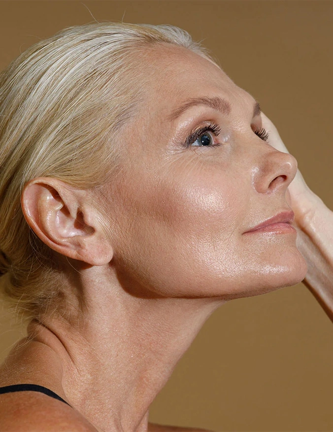 A close up shot of the side of a women's face looking to the right of the image. She has light eyes and blonde hair and her hand Is touching the opposite side of her face. - Mohs Reconstruction in Santa Barbara, CA