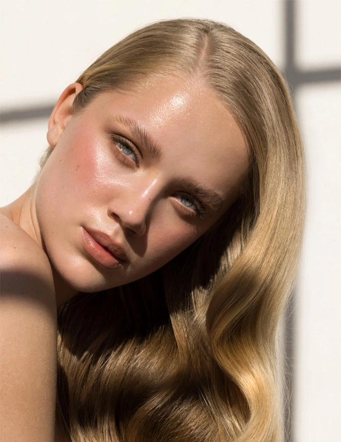 a women in the center from her shoulder up. She has blonde hair with a slight wave and a side part. She is peering over her right shoulder with her lips slightly open. She has grey-blue eyes and glowy-tanned skin. - Neograft in Santa Barbara, CA.