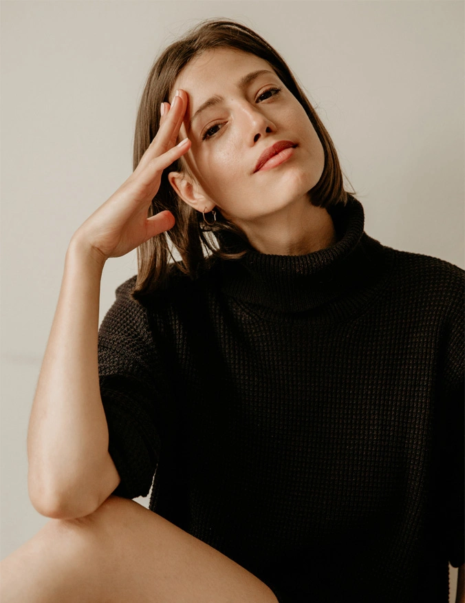 A image of a women wearing a black shirt, her hand is resting against her forehead. She has a brown bob. Her elbow rests upon her knee. - Ulthera Sofwave Eyelid in Santa Barbara, CA